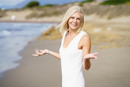 Smiling mature woman walking on the beach  spending her leisure time  enjoying her free time
