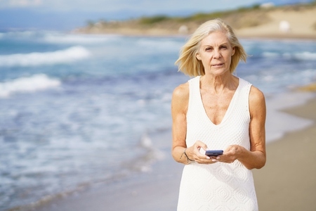 Mature woman walking on the beach using a smartphone