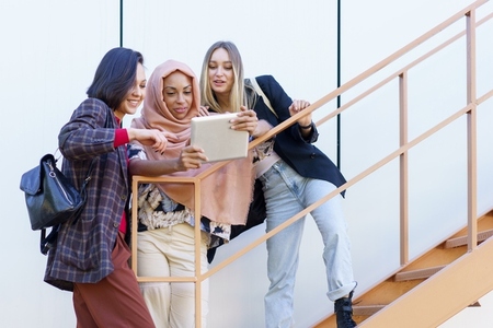 Smiling young diverse ladies using tablet on stairs