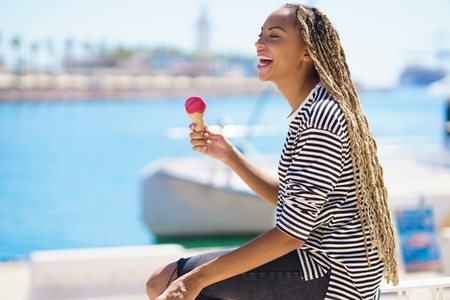 Black woman eating a strawberry ice cream while enjoying the view of the seaport