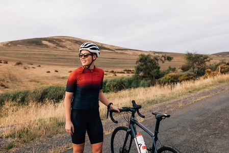 Sportswoman wearing a cycling helmet and sunglasses standing with a bicycle on an empty road
