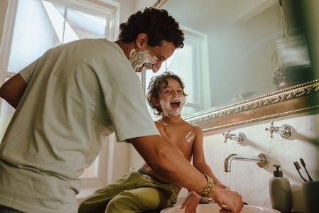 Cheerful father and son having fun with shaving foam