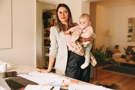 Businesswoman holding her baby while standing in her home office