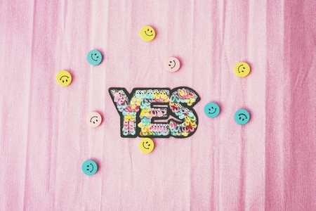 Word yes make with colorful sequins and surrounded by smiley f