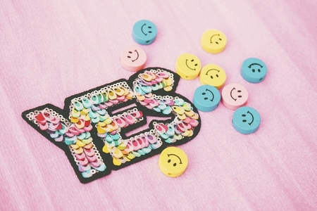 Word yes make with colorful sequins and surrounded by smiley f