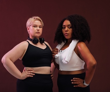 Confident females with plus size bodies standing together in studio and looking at camera