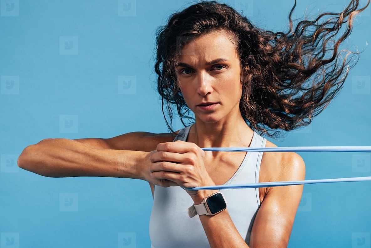 Close up of fit and muscular woman using resistance band against blue background