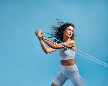 Female athlete working out with stretch bands on blue background  Woman doing intense training using resistance bands