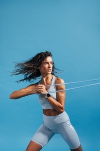Muscular woman exercising against blue background using resistance bands  Fitness female doing strength workout