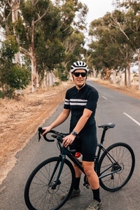 Woman in sportswear wearing helmet and sunglasses standing with road bike