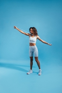 Female in sportswear doing arms stretching workout with resistance band on blue background