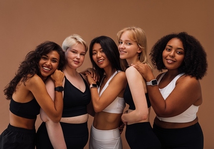 Five women of different body types embracing together  Cheerful females in sport clothes posing on brown background