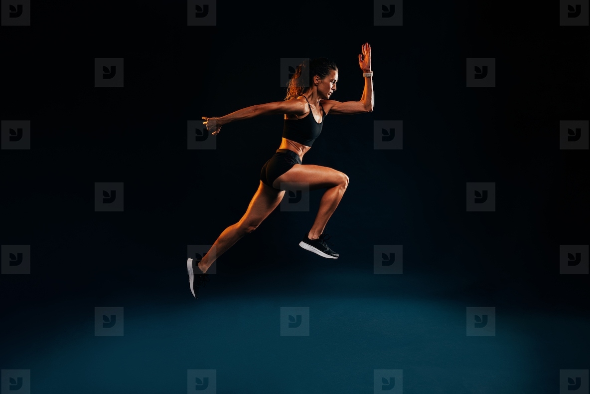 Fit woman running and jumping in the studio. Young female sprinting against dark background.