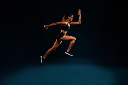 Fit woman running and jumping in the studio  Young female sprinting against dark background