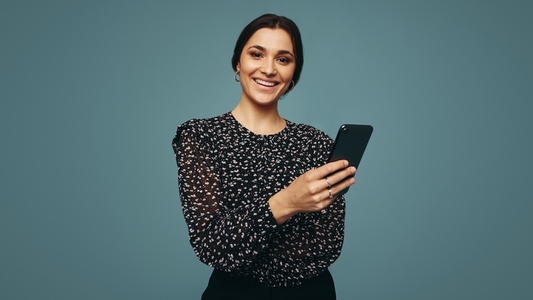 Carefree young woman holding a smartphone in a studio