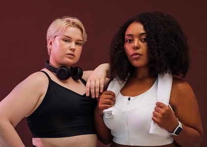 Tow plus size females in fitness attire standing back to back on brown background