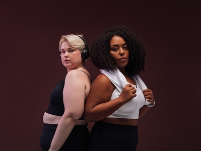 Two female girlfriends in sport bra standing together on brown background  Women in sports clothing standing after workout session