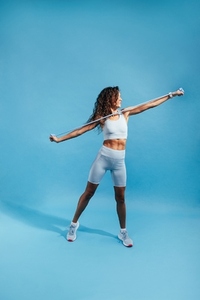 Healthy female in fitness clothes exercising on blue background  Muscular woman working out with resistance band