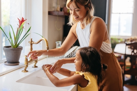 Mother teaching her daughter to wash her hands with soap