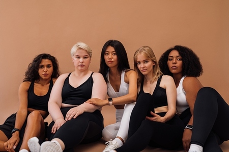 Five women in sportswear sitting together on brown background  Young females of different body types in fitness attire