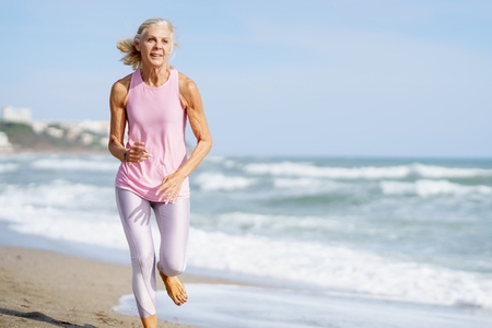 Elderly sportswoman running along seashore in summer