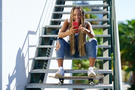 Cheerful black female skater browsing smartphone in city