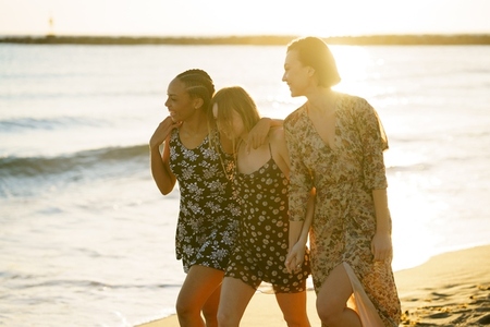 Delighted multiracial girlfriends walking on seashore