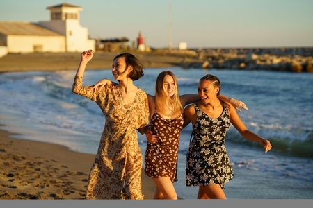 Happy diverse girlfriends walking on sandy beach
