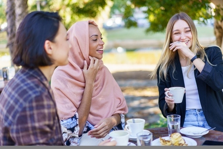 Laughing diverse female friends drinking coffee in outdoor cafe