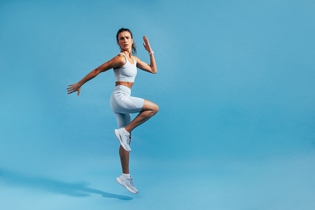 Slim woman jumping in studio on blue background  Muscular female in fitness clothes exercising