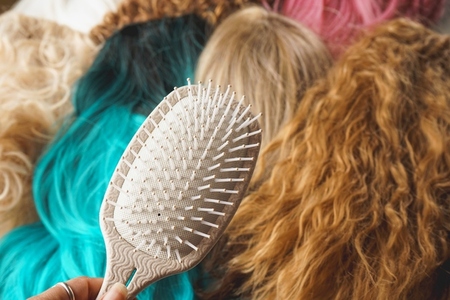 Close up of a hair brush against a background of a lot of wigs