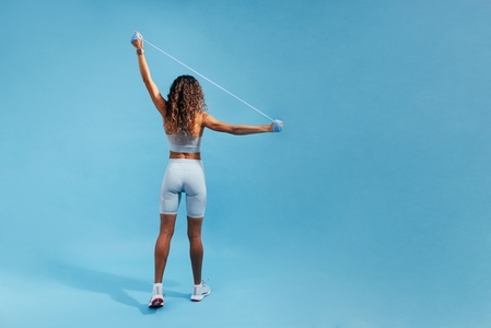 Back view of fit woman standing on blue background doing strength training using resistance bands