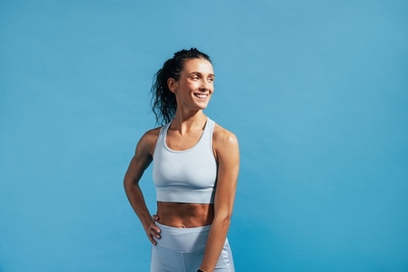 Portrait of a young smiling female in sportswear posing on blue background
