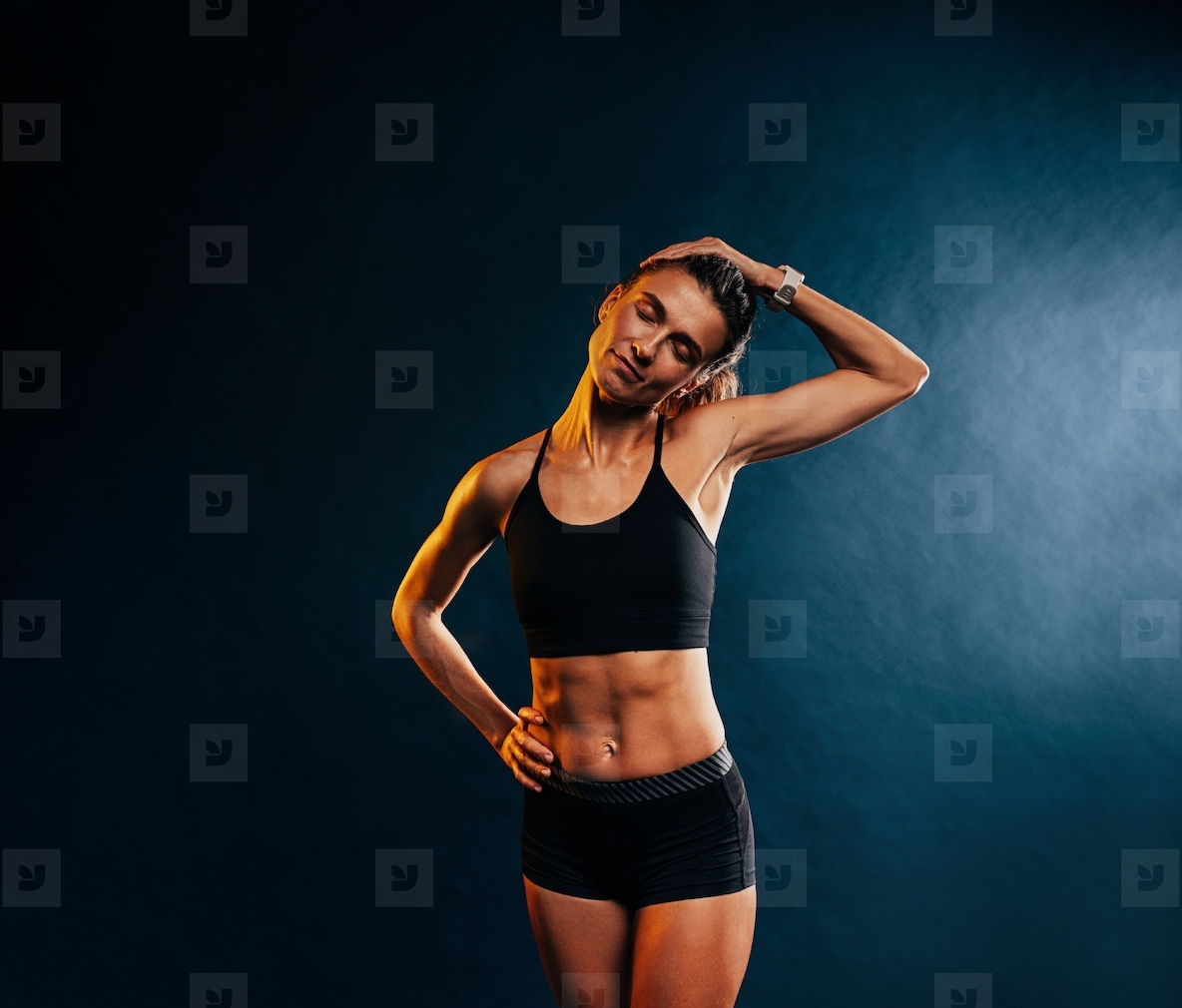 Young muscular woman warming up her neck before training against black background