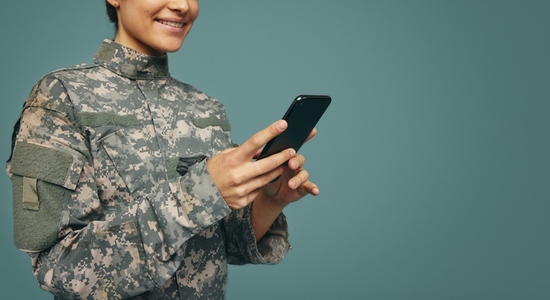 Happy female soldier using a smartphone in a studio