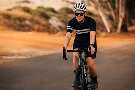 Smiling woman in helmet and sunglasses riding her road bike outdoors