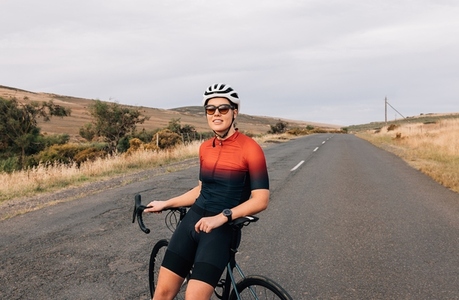 Professional woman cyclist in sunglasses and helmet sitting on bike relaxing after ride