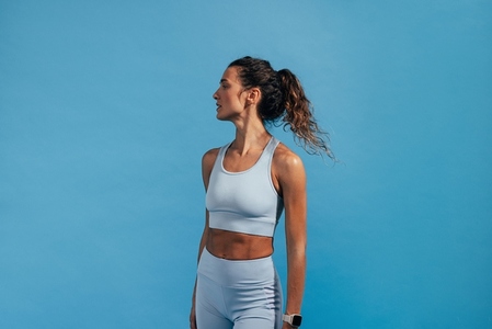 Side view portrait of sportswoman in blue fitness wear  Female athlete standing on blue background