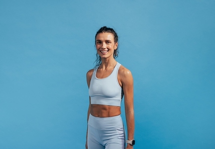 Portrait of young fitness female in sportswear looking at camera while standing on blue background