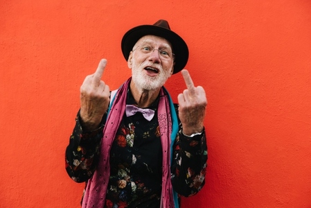 Happy eccentric man showing his middle fingers against a red wall