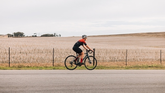 Woman cyclist exercising outdoors on road bike against agriculture field