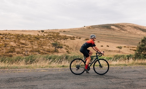 Side view of professional female cyclist in sportswear riding pro bike against beautiful landscape