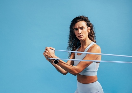 Portrait of young fitness female training with resistance band on blue background