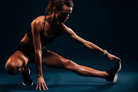 Athlete doing stretching exercises on black background  Female runner stretching leg muscles by touching his shoes while sitting in studio