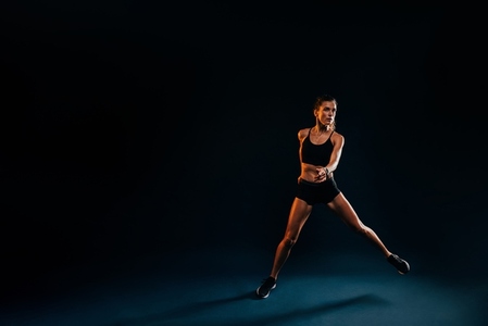 Healthy strong woman jumping from side to side on black background warming up