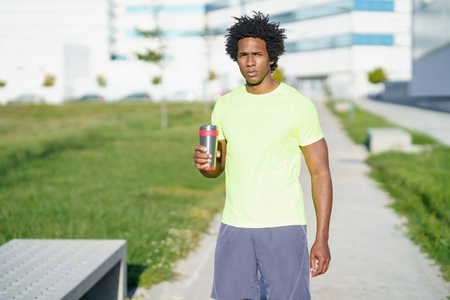 Tired African American sportsman with water in city