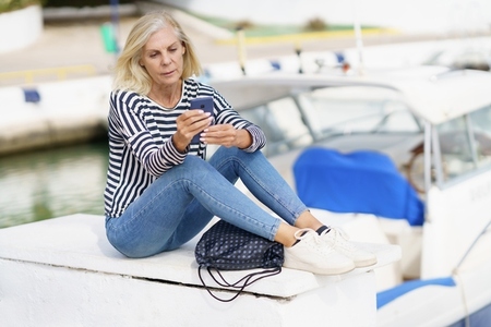 Mature woman using her smartphone sitting in a sea port