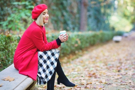Stylish woman with takeaway beverage in autumnal park