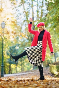 Content woman in elegant wear raising leg in autumn park