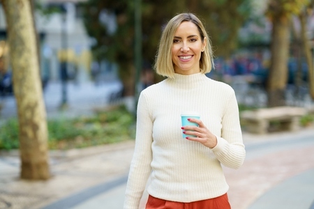 Smiling woman with cup of drink standing on street